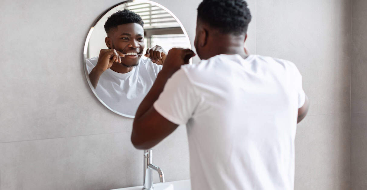 African guy using tooth floss caring for teeth in bathroom flossing is important